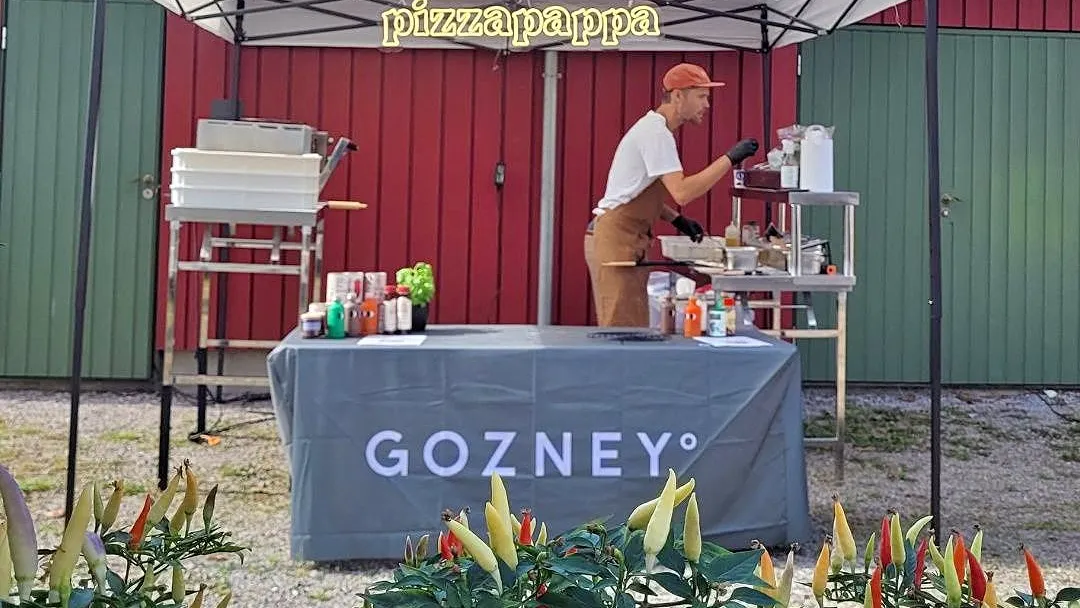 Vegard steker pizza under Pizzapappa-teltet, med chiliplanter i forgrunnen